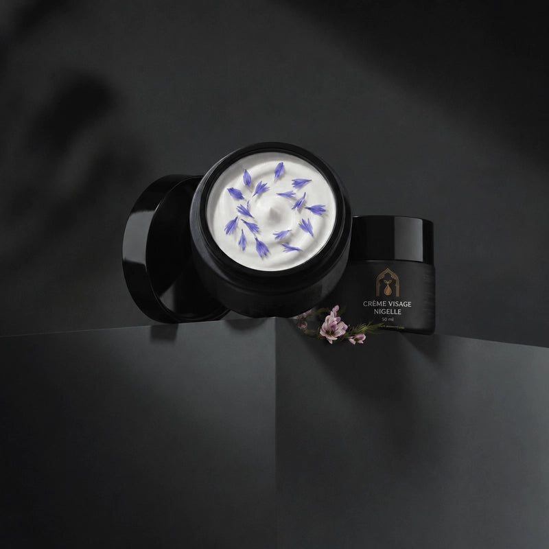 Deux pots de crème visage à la nigelle noirs, pot ouvert montrant de la crème blanche