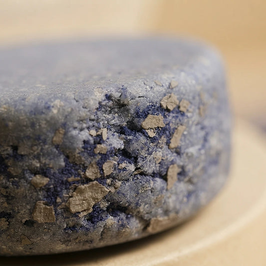 Pain de shampoing solide gris bleuté, texture avec particules bleu foncé et sable
