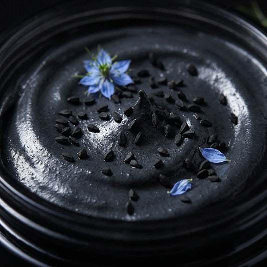 Pot de masque noir au charbon, texture granuleuse, fleurs bleues visibles