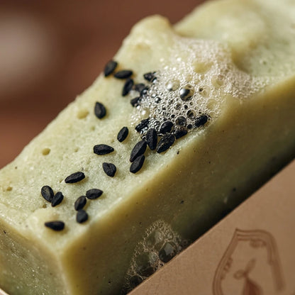 Pain de savon à la nigelle crème avec graines noires, mousse en surface.