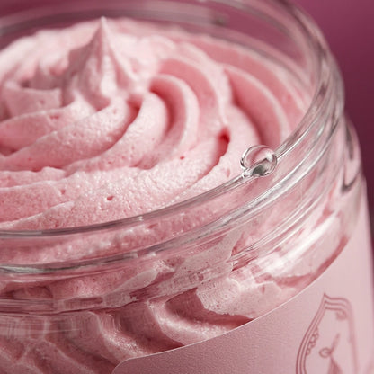 Texture chantilly rose de beurre corporel dans un pot transparent, bord et couvercle visibles.