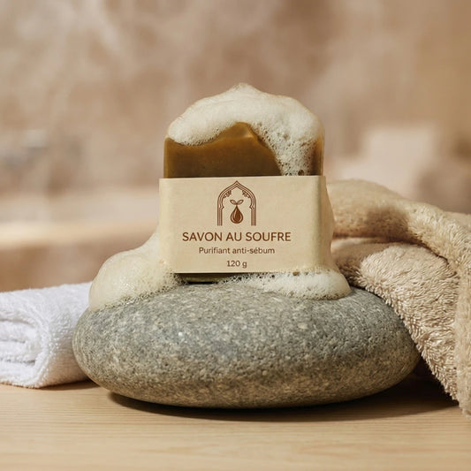 Savon au soufre en pain brun, étiquette crème, mousse blanche; posé sur galet gris.
