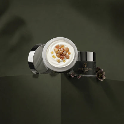 Pot de crème tonifiante ouvert, crème blanche et particules ambrées visibles.