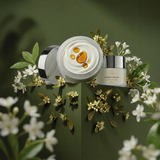 Pot de crème visage à l’argan bio, couvercle ouvert, crème ivoire et gouttes ambrées