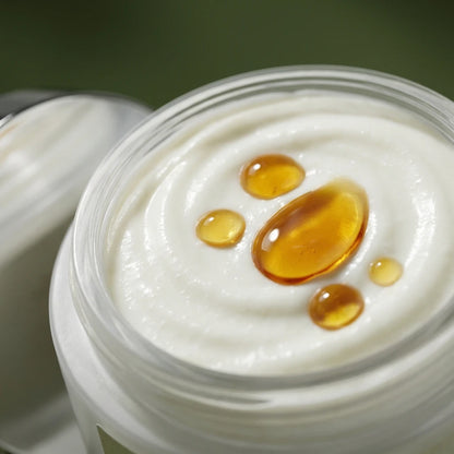Crème visage à l’argan bio dans un pot, texture ivoire avec gouttes d’huile ambrée