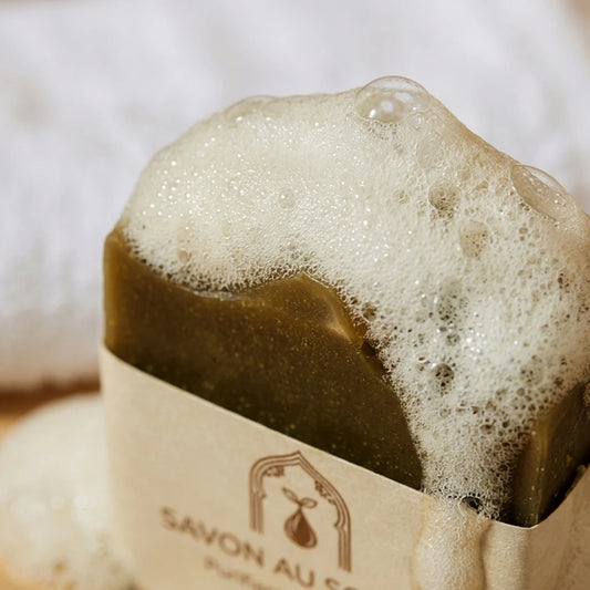 Pain de savon au soufre brun foncé, étiquette crème, mousse blanche en surface.