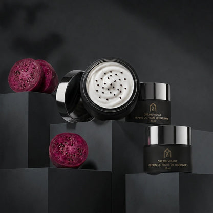 Deux pots de crème visage noirs, couvercles ouverts, crème blanche et graines noires.