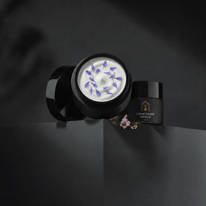 Deux pots de crème visage à la nigelle noirs, pot ouvert montrant de la crème blanche