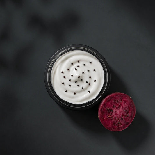 Pot de crème visage noir, couvercle ouvert, crème blanche avec graines noires.