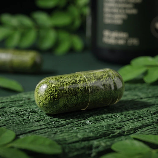 Gélule de moringa verte, capsule végétale posée sur une planche en bois.