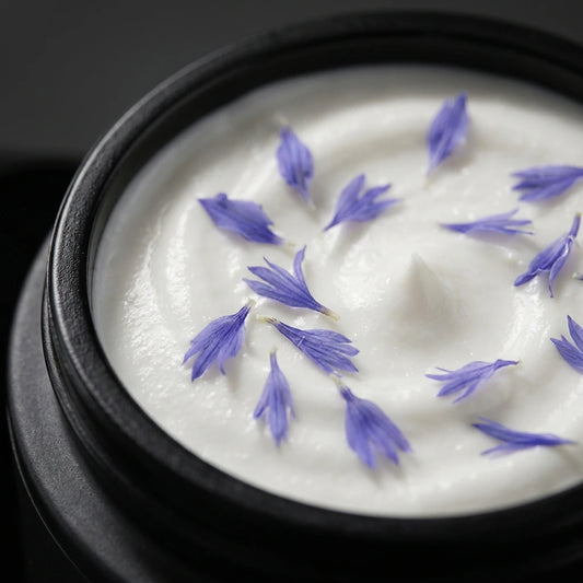 Pot de crème visage à la nigelle noir, crème blanche parsemée de fleurs violettes