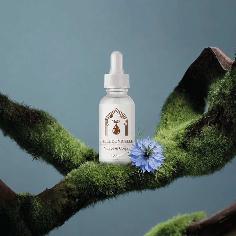 Flacon d’huile de nigelle 100 ml au milieu de mousse et d’une fleur bleue.