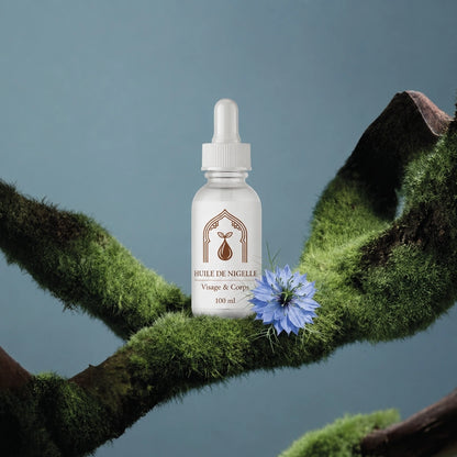 Flacon d’huile de nigelle 100 ml au milieu de mousse et d’une fleur bleue.