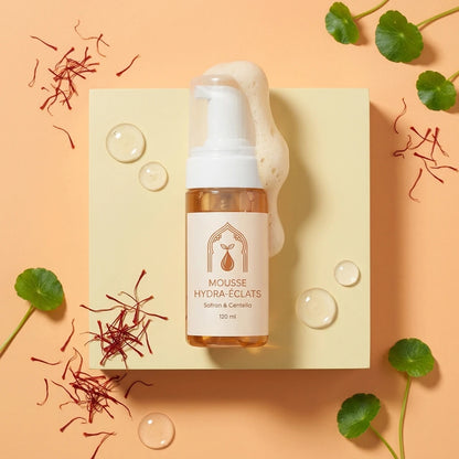 Flacon-pompe mousse hydra-éclats sur fond clair, feuilles vertes et safran rouge autour
