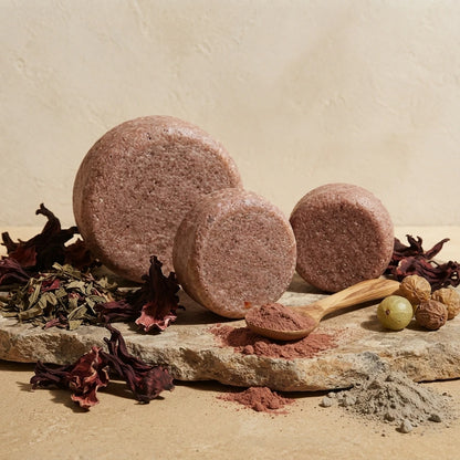 Shampoing solide brun, plusieurs pastilles et cuillère en bois sur une pierre.